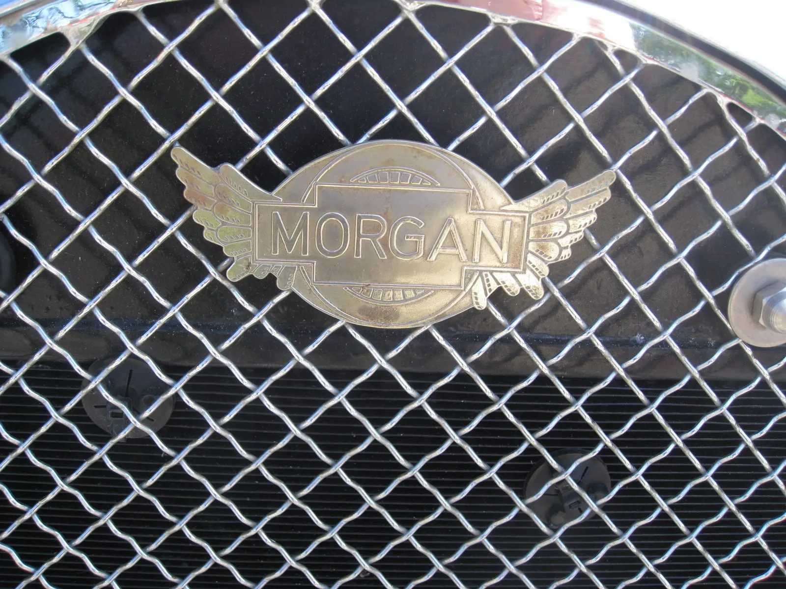 A winged Morgan badge on a chrome mesh radiator grille