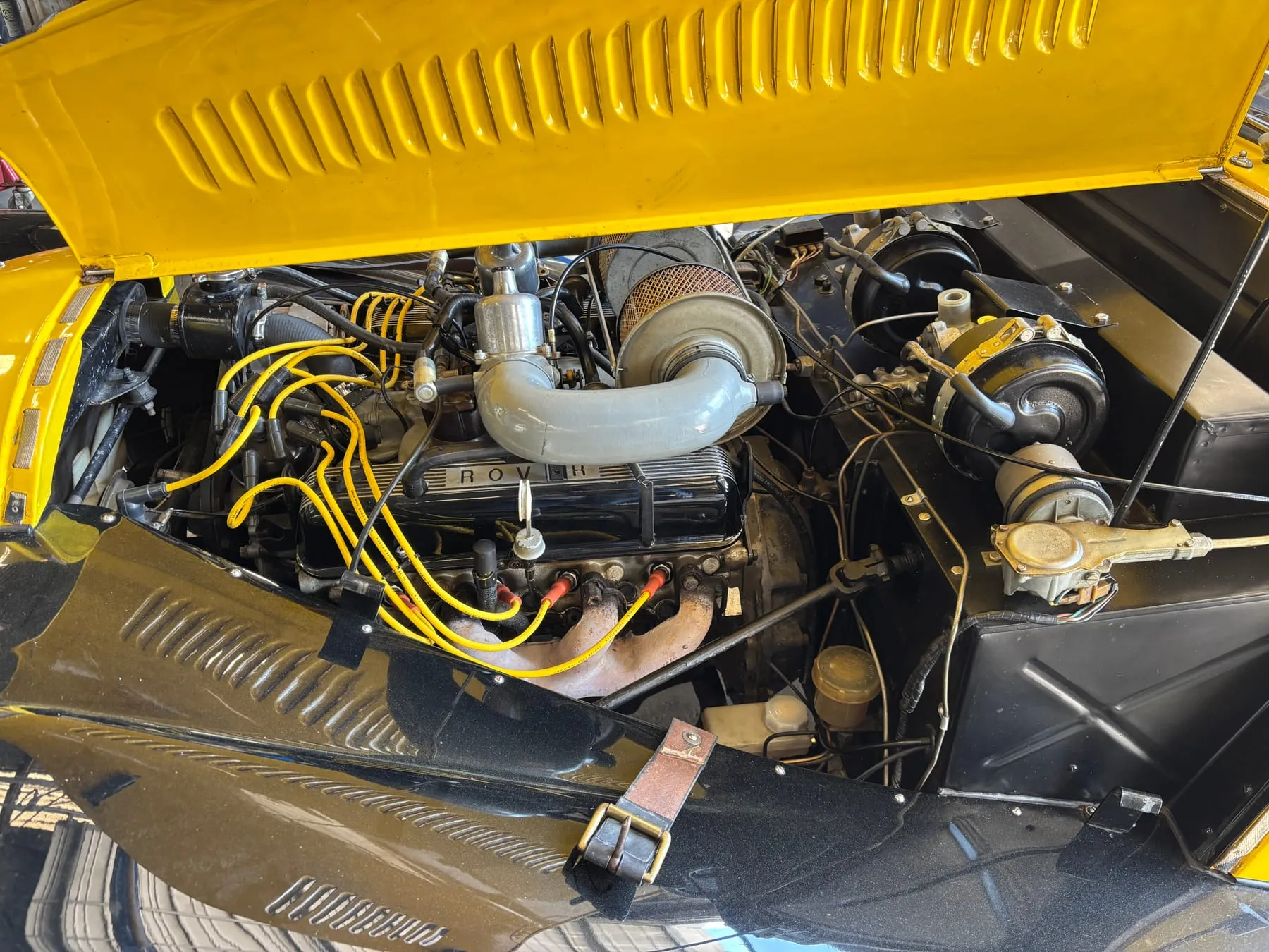 Under the bonnet of the yellow 1971 Plus 8: the engine, yellow plug leads and chrome air pipes