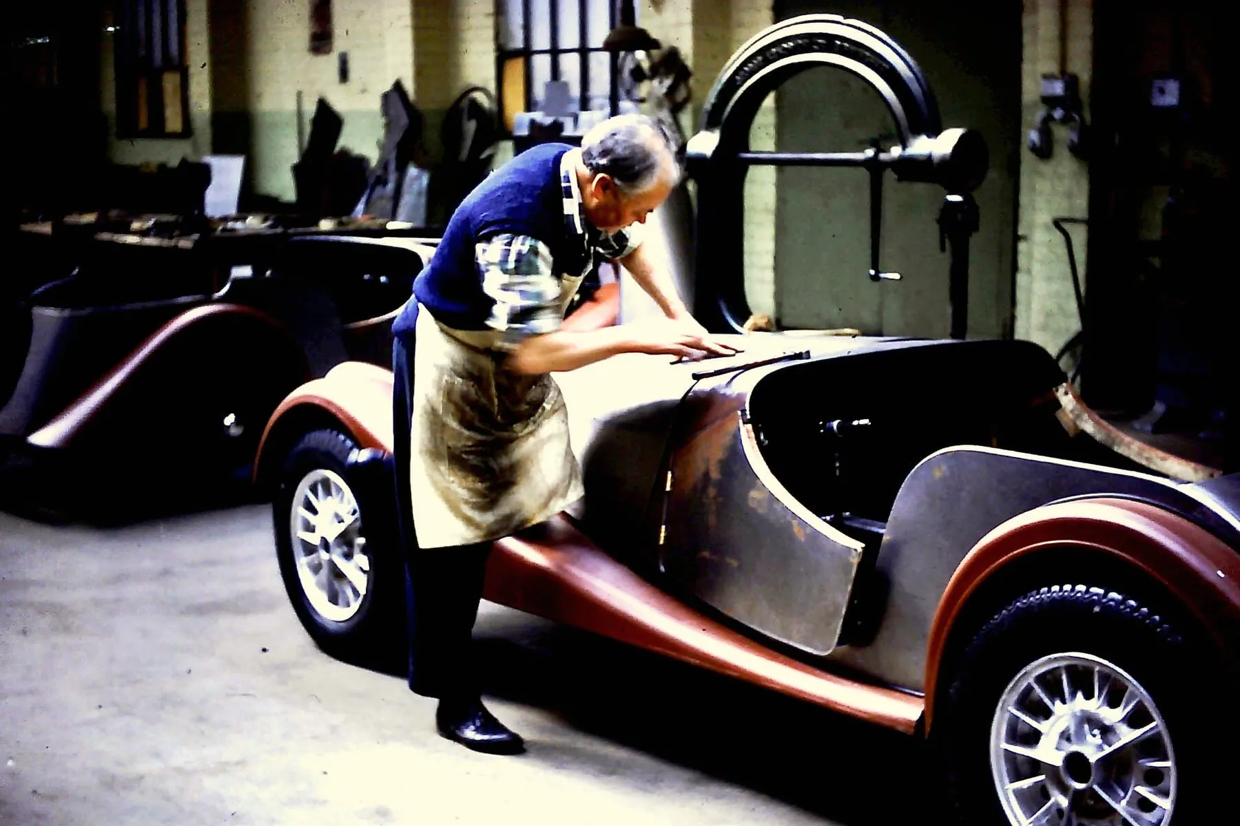 A worker fitting a bonnet to a partly assembled Morgan inside the works