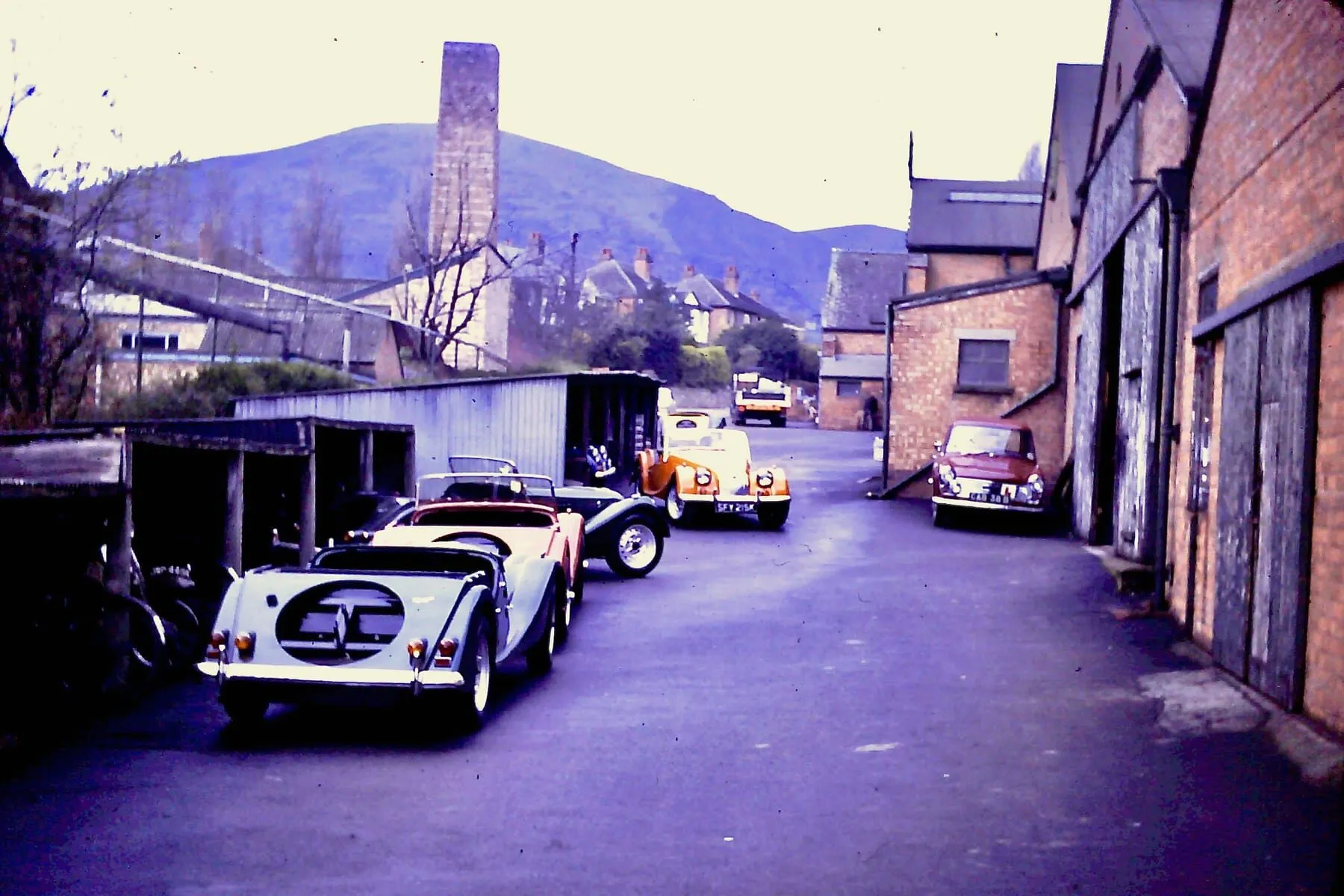 A narrow lane beside the Morgan works, with several Morgans parked along it
