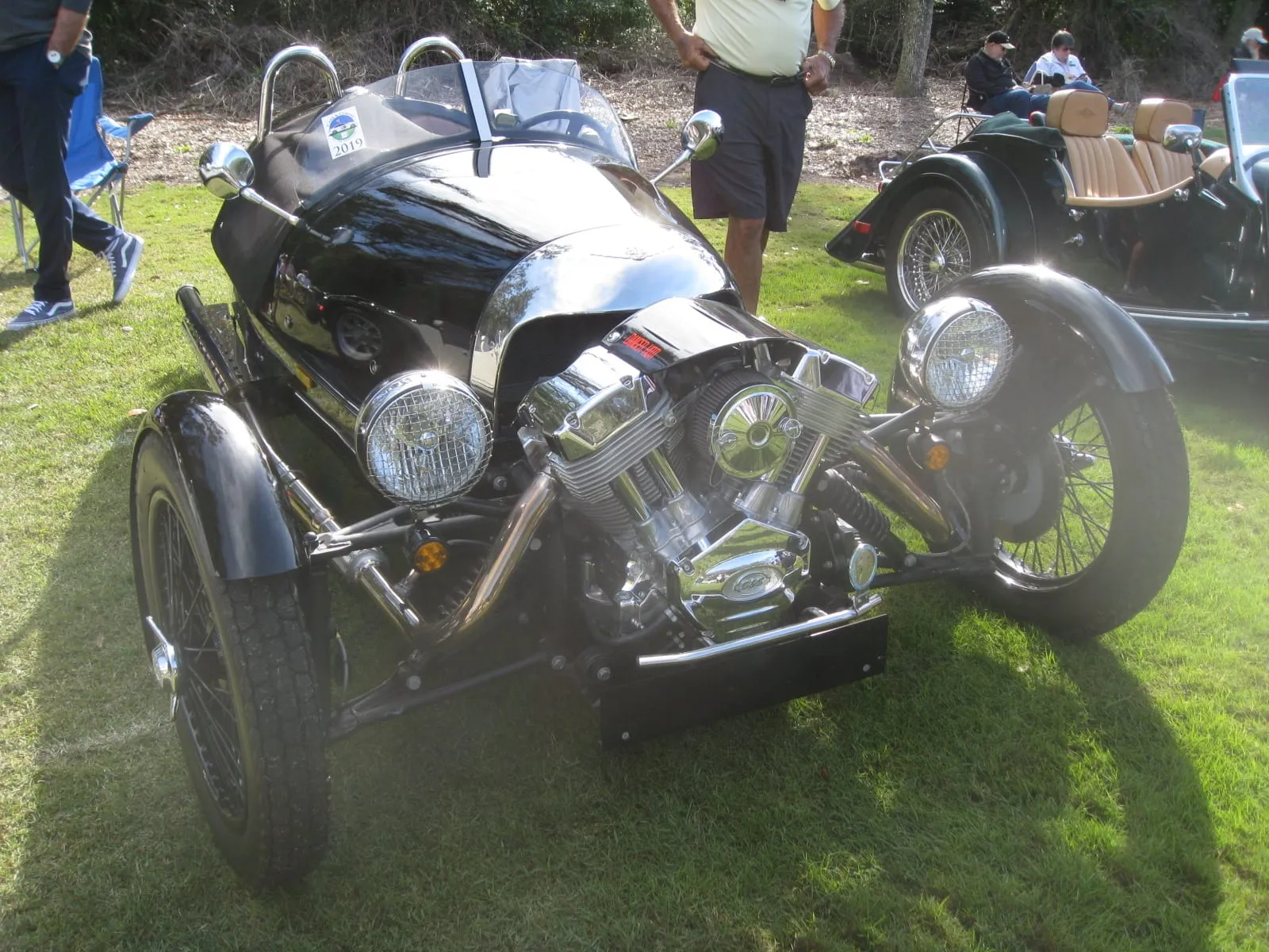 A black three-wheeler with its V-twin engine bare at the front, on a lawn