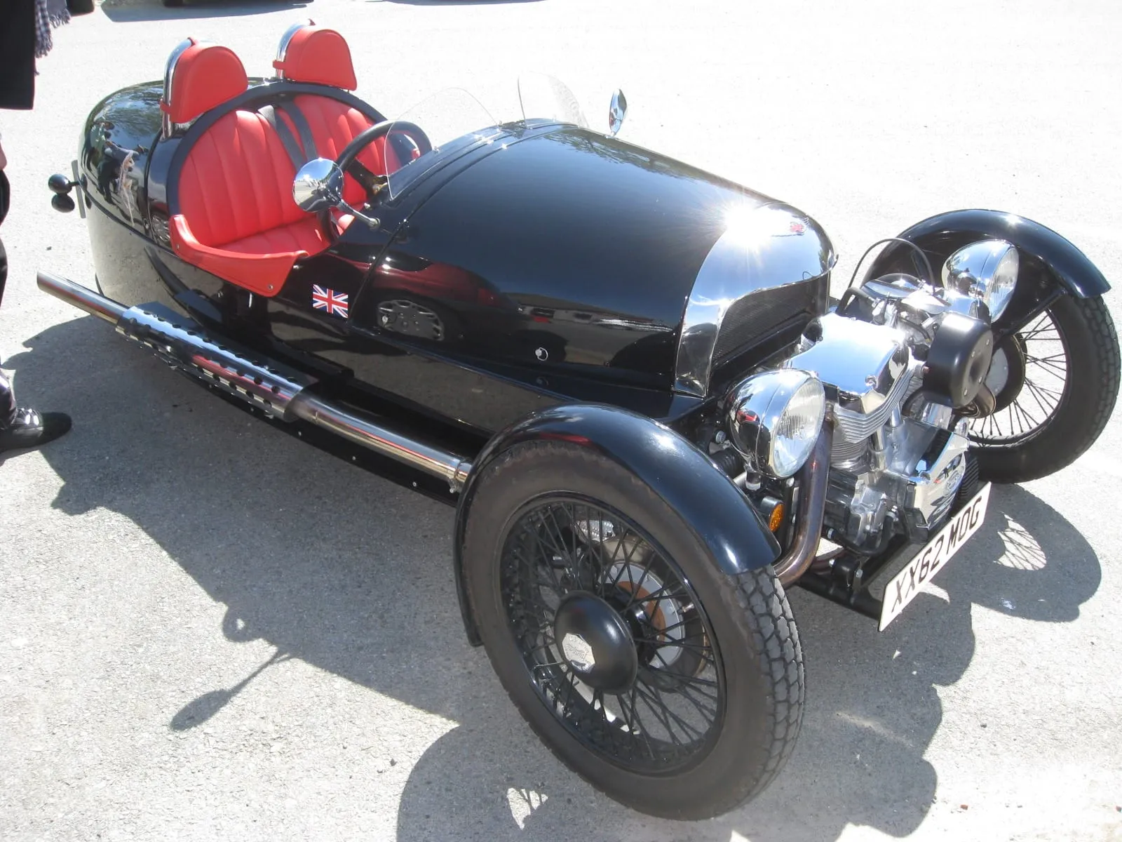 A black 2011 three-wheeler with red seats and a V-twin engine out in front, a small Union flag on its tail
