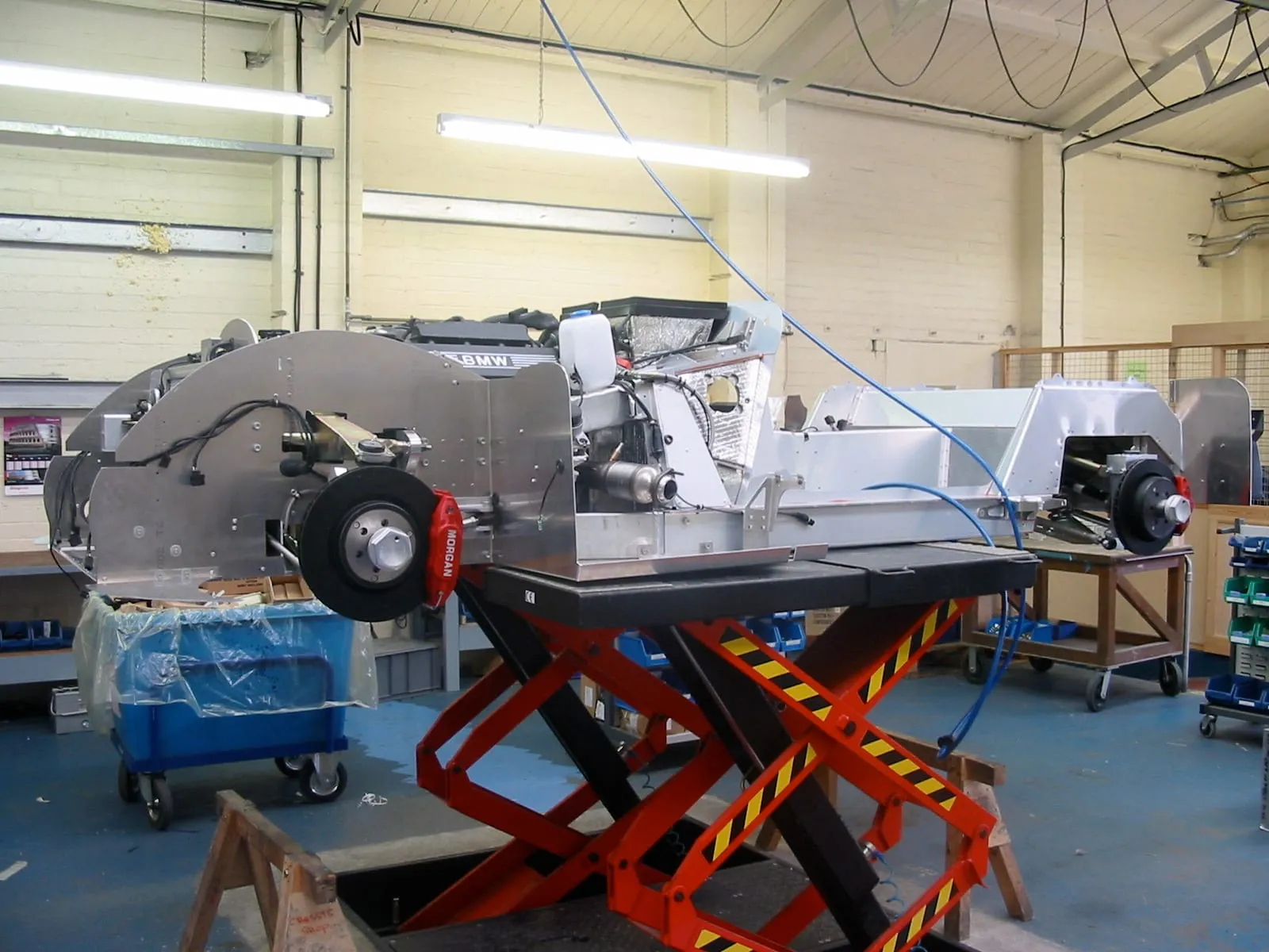 An Aero 8 chassis on a red scissor lift, with its BMW V8 fitted