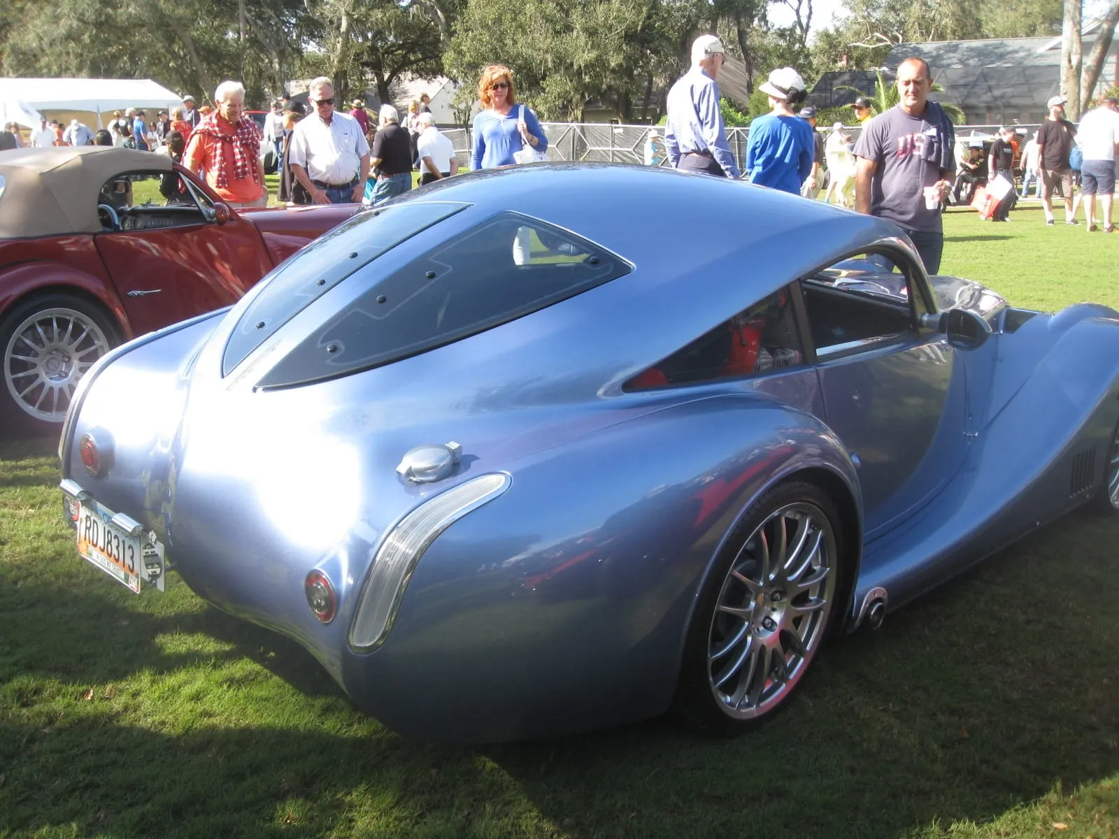 The rear three-quarter view of the pale blue Aero Coupé on a lawn, with its sloping glass hatch