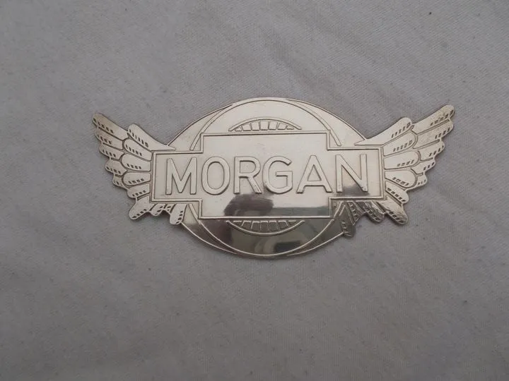 A polished winged badge with MORGAN across the middle, lying on grey cloth