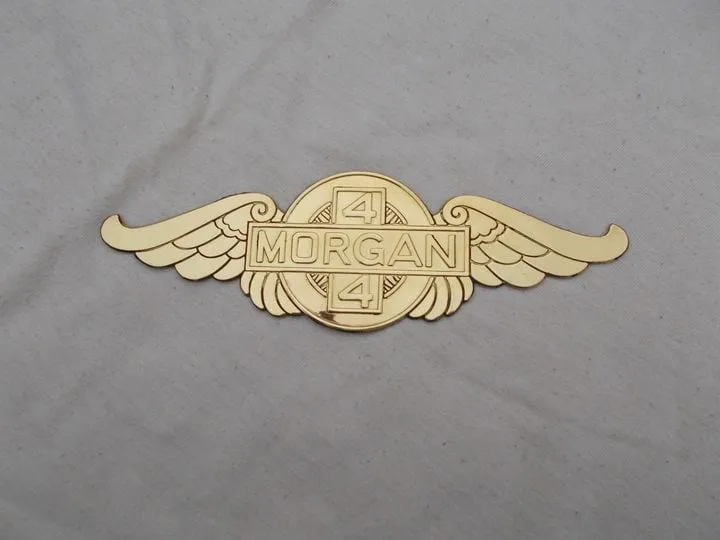 A brass winged badge with MORGAN on a bar between two number 4s, lying on grey cloth