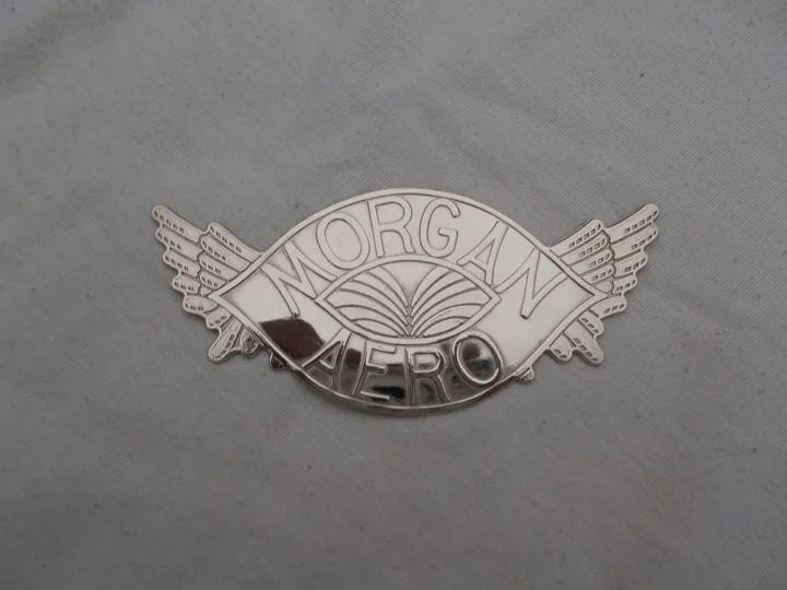 A polished winged badge reading MORGAN above AERO, lying on grey cloth