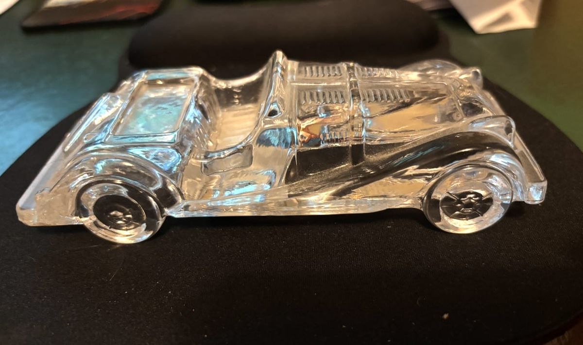 A clear glass model of an open Morgan roadster on a black desk mat