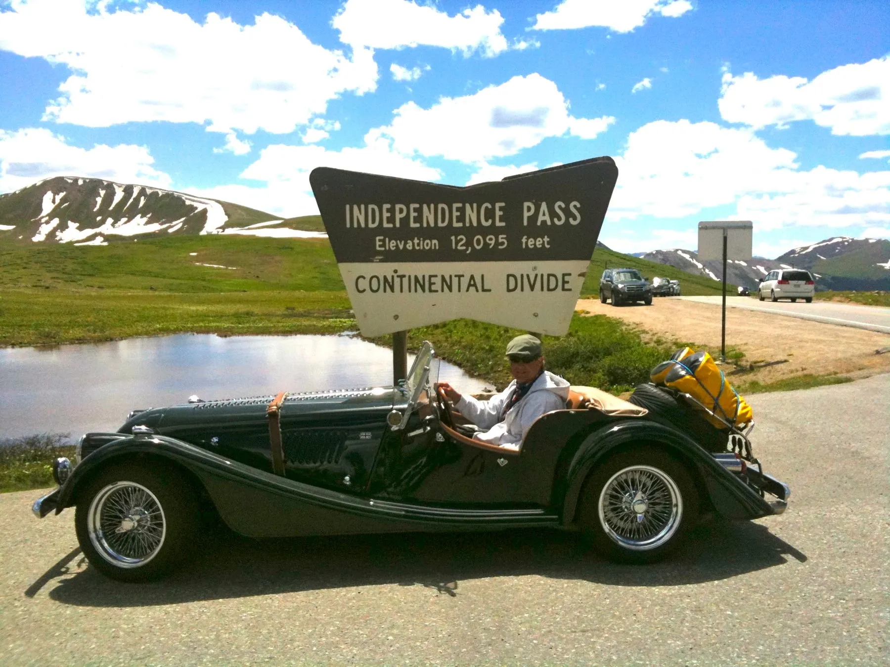 A man sitting in a dark Morgan below the Independence Pass sign on the Continental Divide