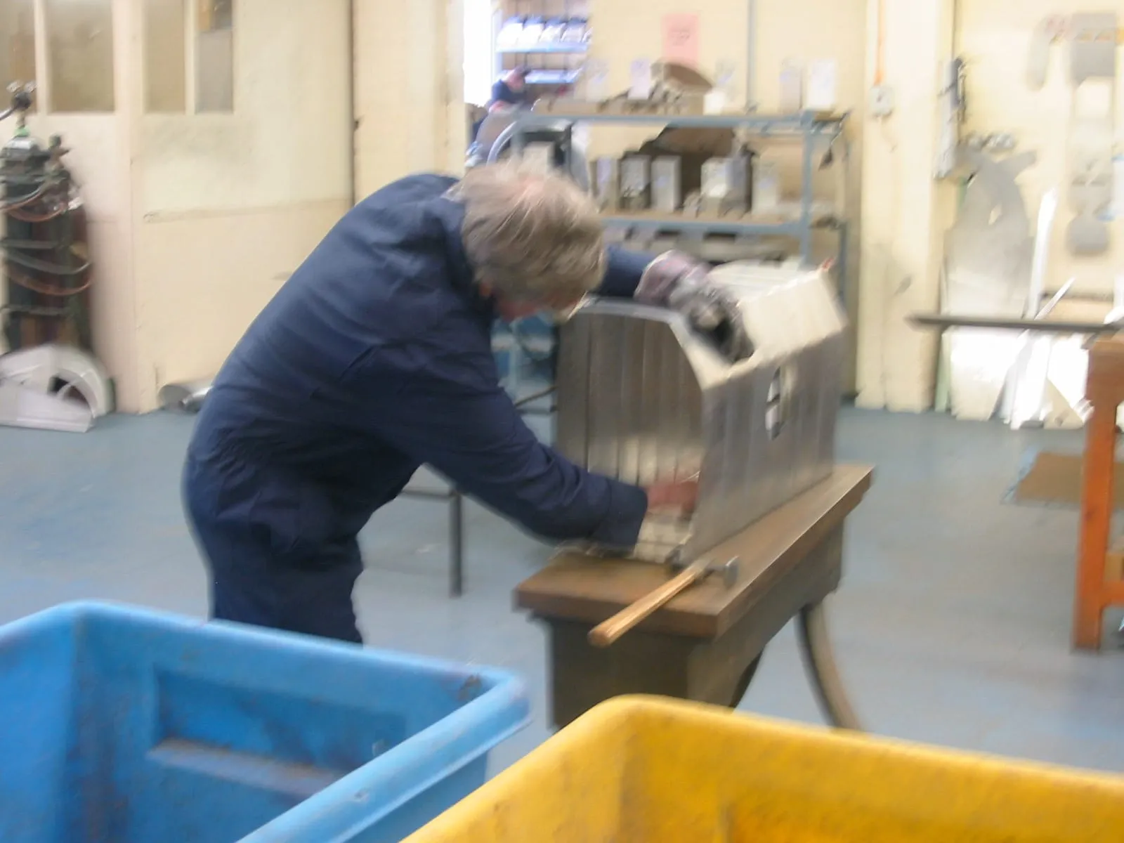 A man in a dark overall shaping a metal fuel tank at a bench