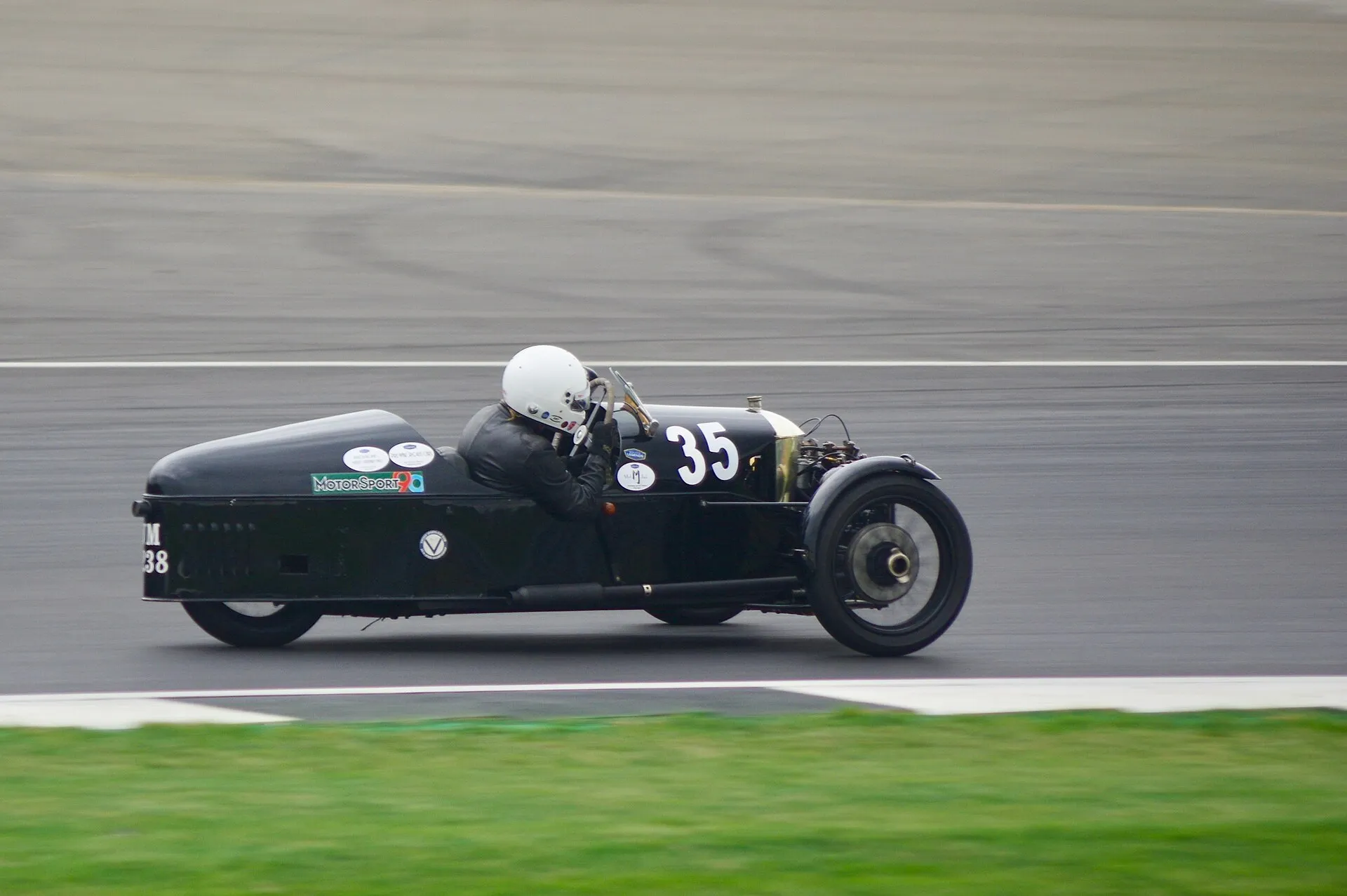 A dark 1929 Morgan Super Aero three-wheeler racing on a circuit