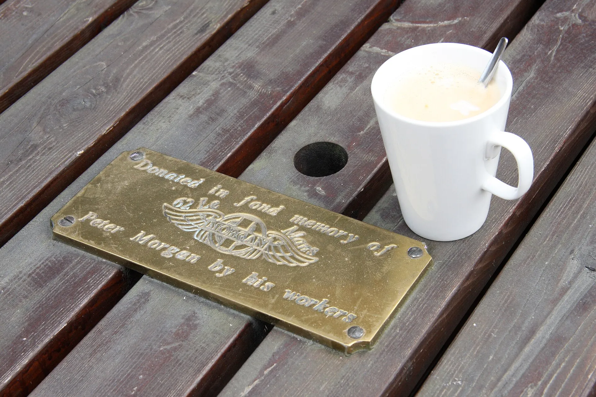 A small brass plaque on a wooden bench reading "Donated in fond memory of Peter Morgan by his workers"