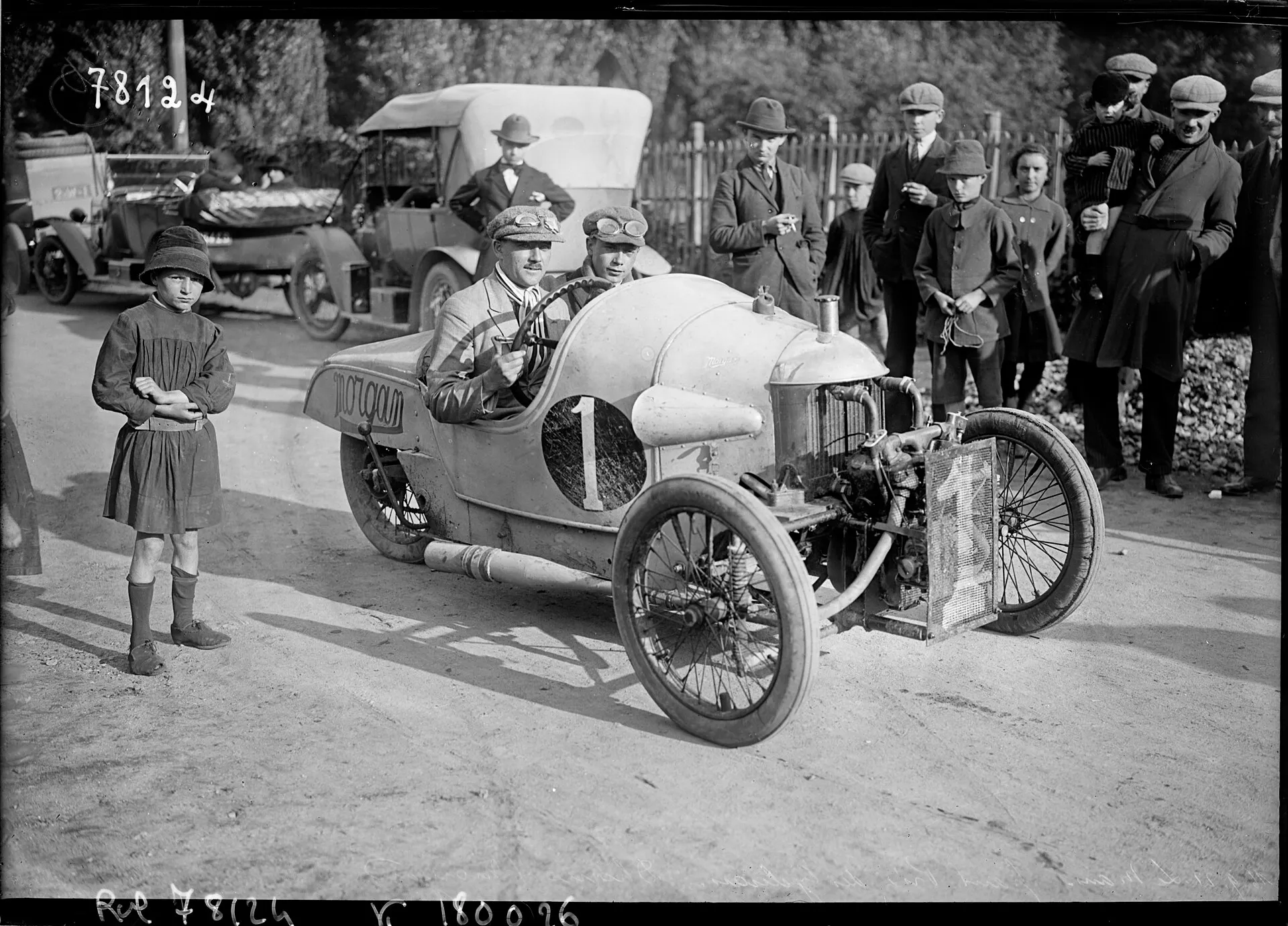 A black-and-white press photograph of a Morgan cyclecar with a long streamlined tail at the weigh-in, with a boy and onlookers