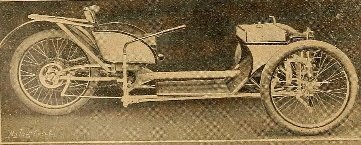 A 1910 photograph of the bare chassis of a Morgan three-wheeler seen from the side, with long footboards, a tiller-style control lever, a small low seat, one large rear wheel and a spoked front wheel