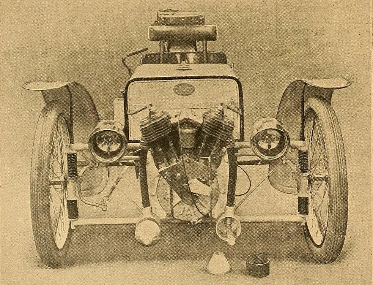 A 1910 studio photograph of a Morgan three-wheeler from the front: a J.A.P. V-twin engine between two lamps, a wheel and splayed mudguard on each side, and a single narrow seat behind a flat bonnet