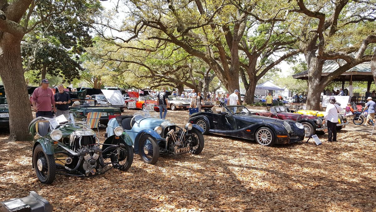 Vintage three-wheelers and sports cars parked under live oaks at a British car show
