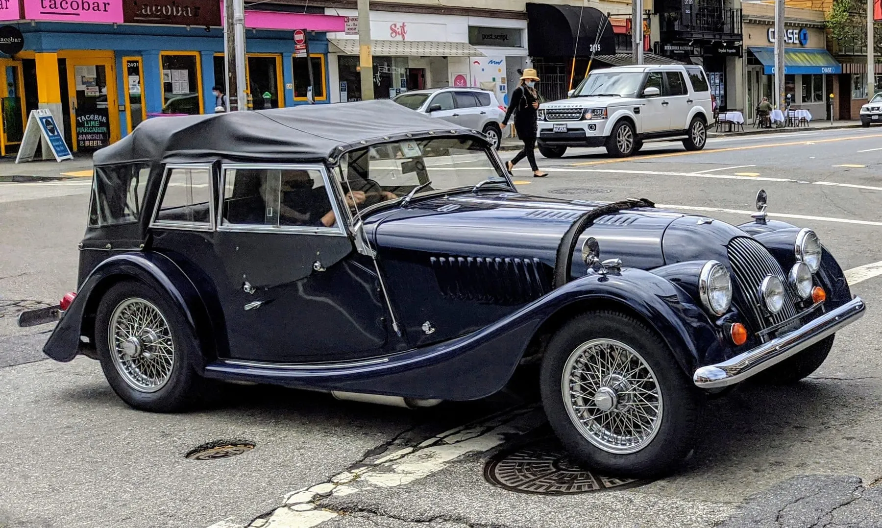 A dark-blue Plus 4 four-seater with its hood up, parked in a San Francisco street