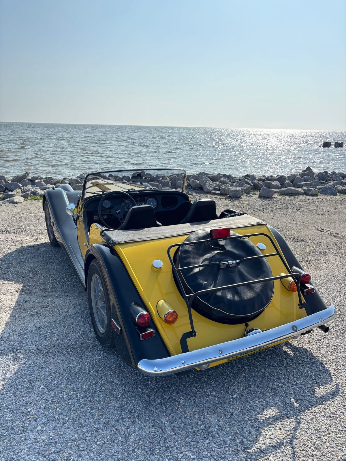 The yellow and black Plus 8 seen from behind at the edge of the sea, its spare wheel on the tail
