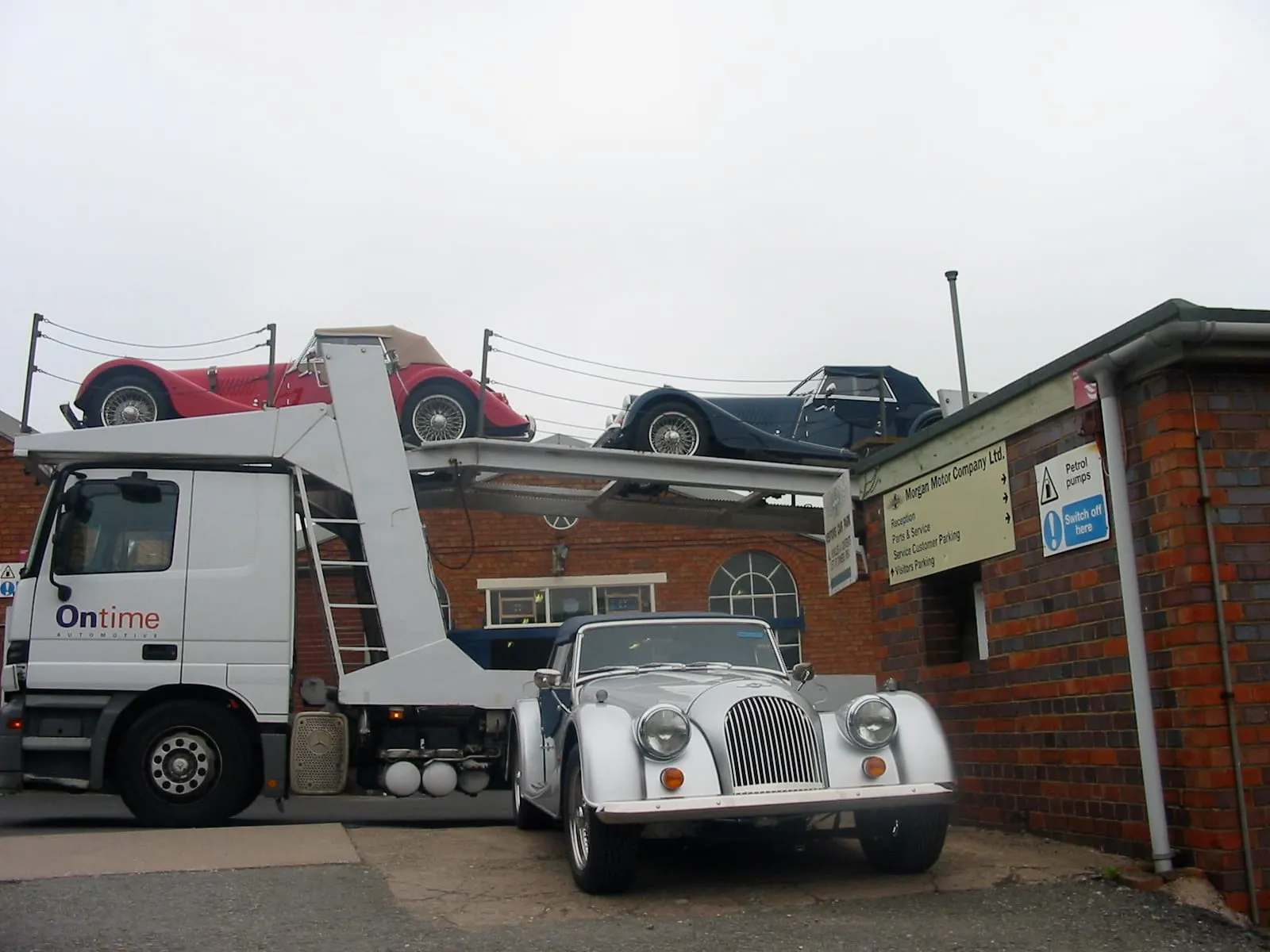 A car transporter loaded with Morgans beside a white Morgan, outside the works