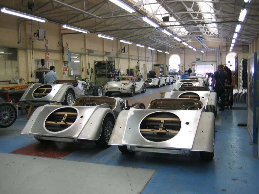 A long shop floor with rows of bare aluminium bodies on trestles
