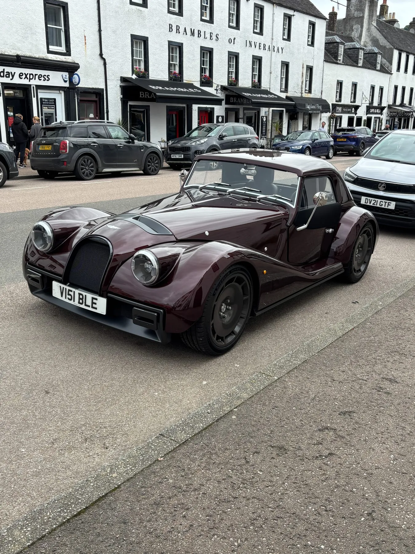 A dark maroon Morgan coupé with a hardtop on a town street